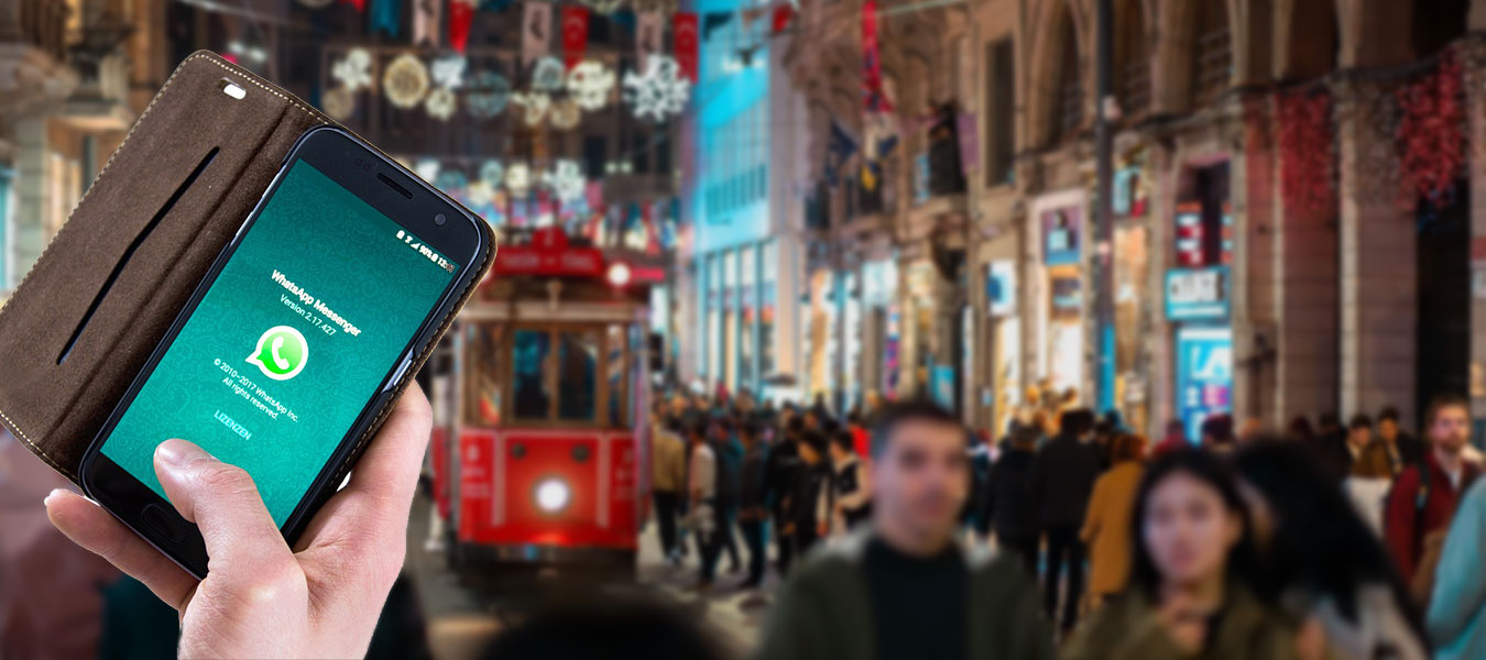 A blurred view of Istiklal Street with red tram and a hand holding a phone showing WhatsApp screen