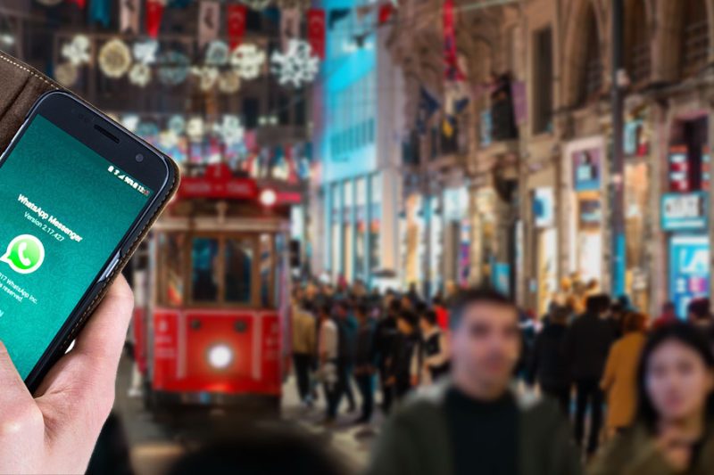 A blurred view of Istiklal Street with red tram and a hand holding a phone showing WhatsApp screen
